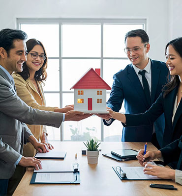 Four persons standing and holding a dummy house with happy faces